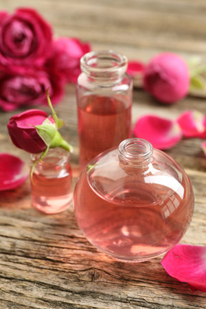 Open perfume bottles with aromatic essential oils and roses on wooden table, closeupの写真素材