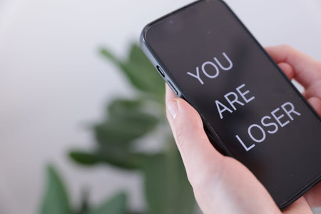 Cyber bullying. Woman holding smartphone with text You Are Loser on blurred background, closeup....