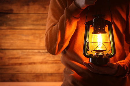 Man with vintage kerosene lamp on wooden background, closeup. Space for textの写真素材