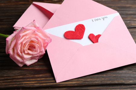 Love letter, envelopes, beautiful rose and red hearts on wooden table, closeup