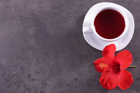 Tasty hibiscus tea in cup and beautiful flower on grey textured table, flat lay. Space for textの写真素材