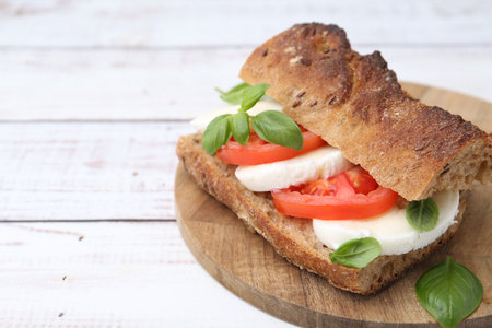 Tasty sandwich with mozzarella cheese, tomatoes and basil on white wooden table, closeup. Space for textの写真素材