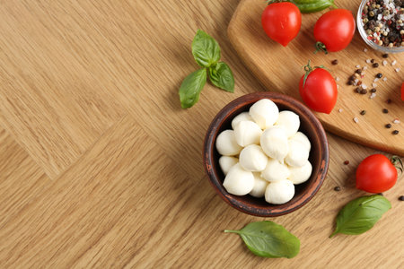 Tasty mozzarella balls, tomatoes, peppercorns and basil on wooden table, flat lay. Space for textの写真素材