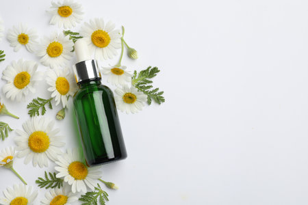 Bottle of essential oil and chamomile flowers on white background, flat lay. Space for textの写真素材