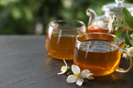 Tasty jasmine tea in cups, teapot and flowers on black table, closeup. Space for textの写真素材