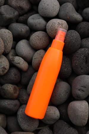 Bottle of sun protection product on pebbles, top view