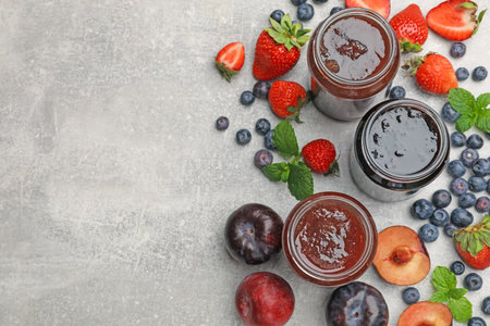 Different sweet jams in jars and ingredients on gray table, flat lay. Space for textの写真素材
