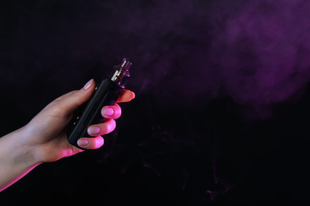 Woman using electronic smoking device in neon lights on black background, closeup. Space for textの写真素材