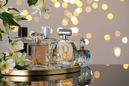 Many different perfume bottles and flowers on mirror surface against light gray background with...