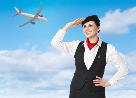 Smiling stewardess against blue sky with plane and cloudsの写真素材