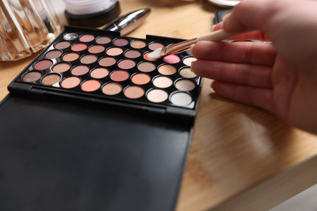 Woman with brush and eyeshadow palette at wooden vanity indoors, closeupの写真素材