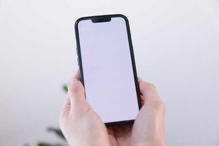 Woman holding smartphone with blank screen on blurred background, closeup. Mockup for designの写真素材