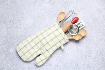 Different kitchen utensils in oven mitten on light table, top viewの写真素材