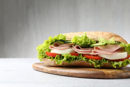 Tasty baguette sandwich with ham and vegetables on light gray table, closeupの写真素材