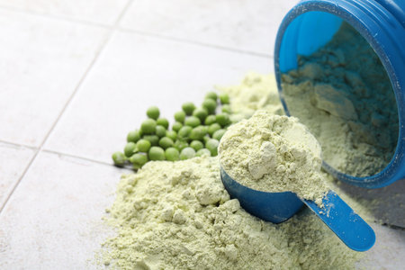 Protein powder and green peas on light tiled table, closeup. Space for textの写真素材