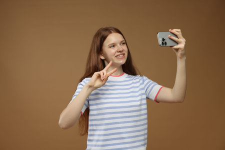 Teenage girl taking selfie on brown background