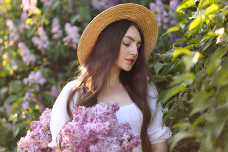 Beautiful woman among lilac flowers and leaves outdoors
