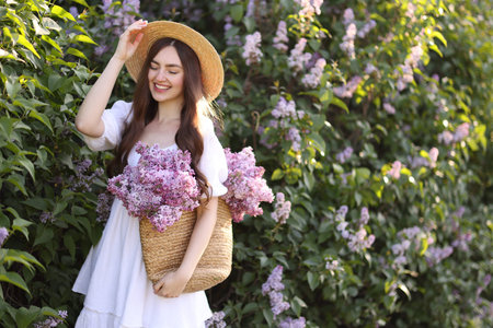 Smiling woman with bag of lilac flowers near bush outdoorsの写真素材
