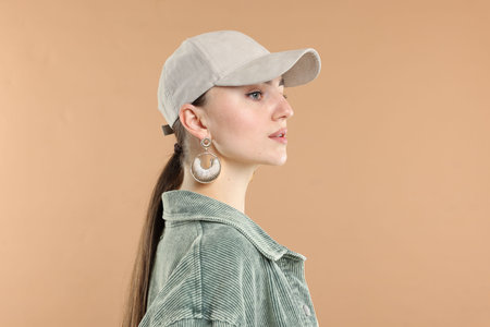 Beautiful woman in stylish baseball hat on beige background