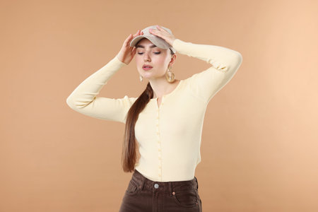 Beautiful woman in stylish baseball hat posing on beige background