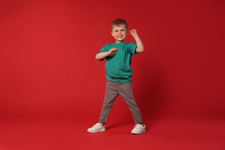 Happy little boy dancing on red background, space for textの写真素材