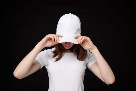 Young woman wearing stylish white baseball hat on black backgroundの写真素材