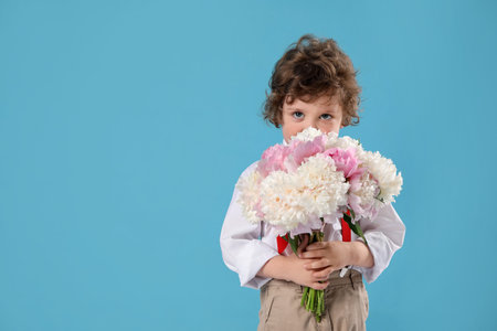 Cute little boy with bouquet of beautiful peonies on light blue background. Space for textの写真素材