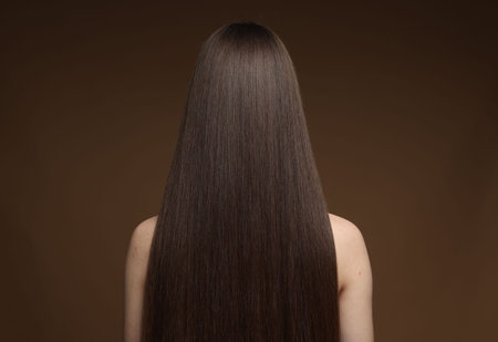 Teenage girl with healthy long hair on brown background, back viewの写真素材