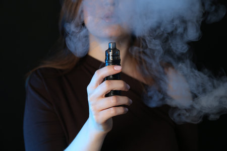 Woman using electronic smoking device on black background, closeupの写真素材