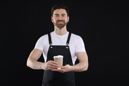 Portrait of smiling barista with takeaway paper cup of hot drink on black background