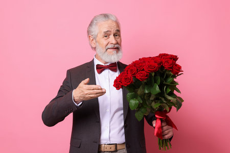 Senior man with bouquet of red roses on pink background