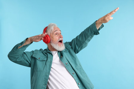 Elderly man in headphones on light blue backgroundの写真素材