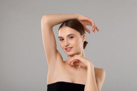 Young woman showing smooth skin after epilation on gray backgroundの写真素材