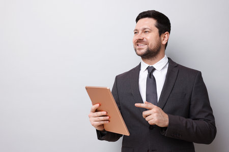 Smiling businessman with tablet on light grey background. Space for textの写真素材