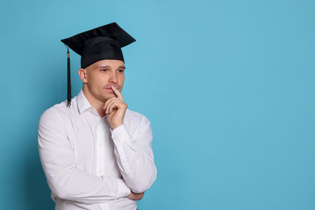 Thoughtful student after graduation on light blue background. Space for textの写真素材