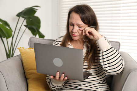 Woman with vision problem using laptop in armchair at homeの写真素材