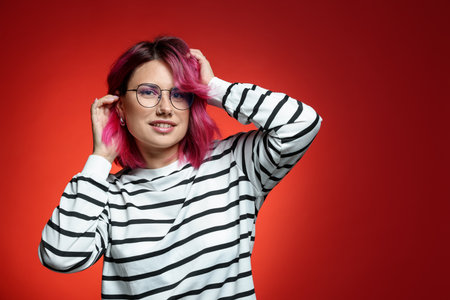 Beautiful woman with pink dyed hair in glasses on red gradient backgroundの写真素材