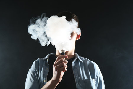 Man using electronic smoking device on black backgroundの写真素材