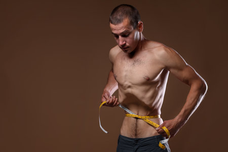 Man measuring his waist on beige background. Space for textの写真素材