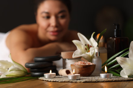 Beautiful woman relaxing on massage couch indoors, focus on different spa products and lily flowersの写真素材