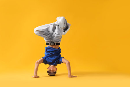 Boy in stylish clothes dancing on yellow background, space for text