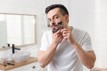 Handsome man shaving with razor in bathroomの写真素材