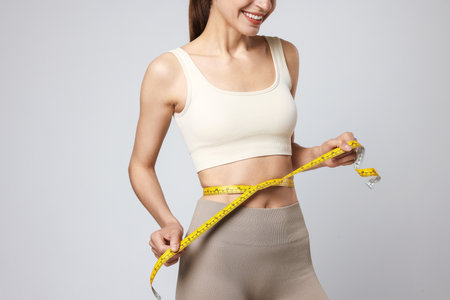 Woman measuring her belly with tape on gray background, closeupの写真素材