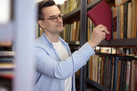 Man taking book from shelf in public libraryの写真素材