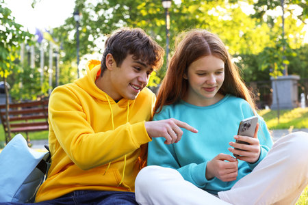 Teenage girl and boy with smartphone in parkの写真素材