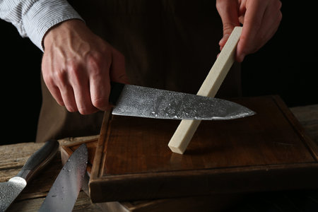 Man sharpening knife with sharpener on wooden table, closeup