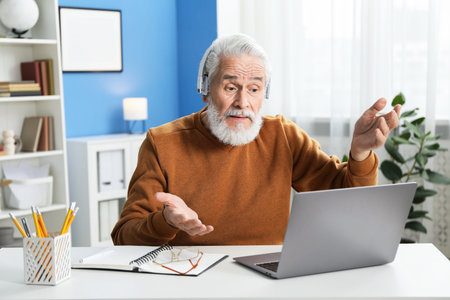 Senior man having online lesson with teacher at desk indoors. Self-study