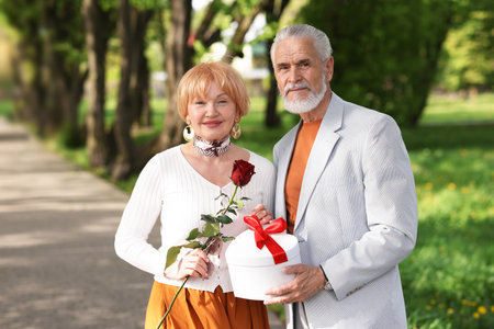 Lovely senior couple with gift box and rose in parkの写真素材