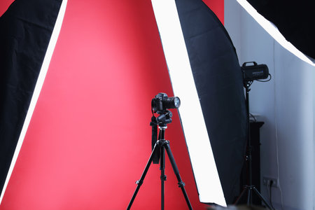 Modern video camera and professional lighting equipment on red backgroundの写真素材