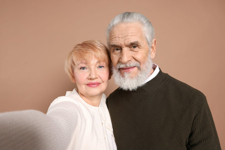 Lovely senior couple taking selfie on beige background